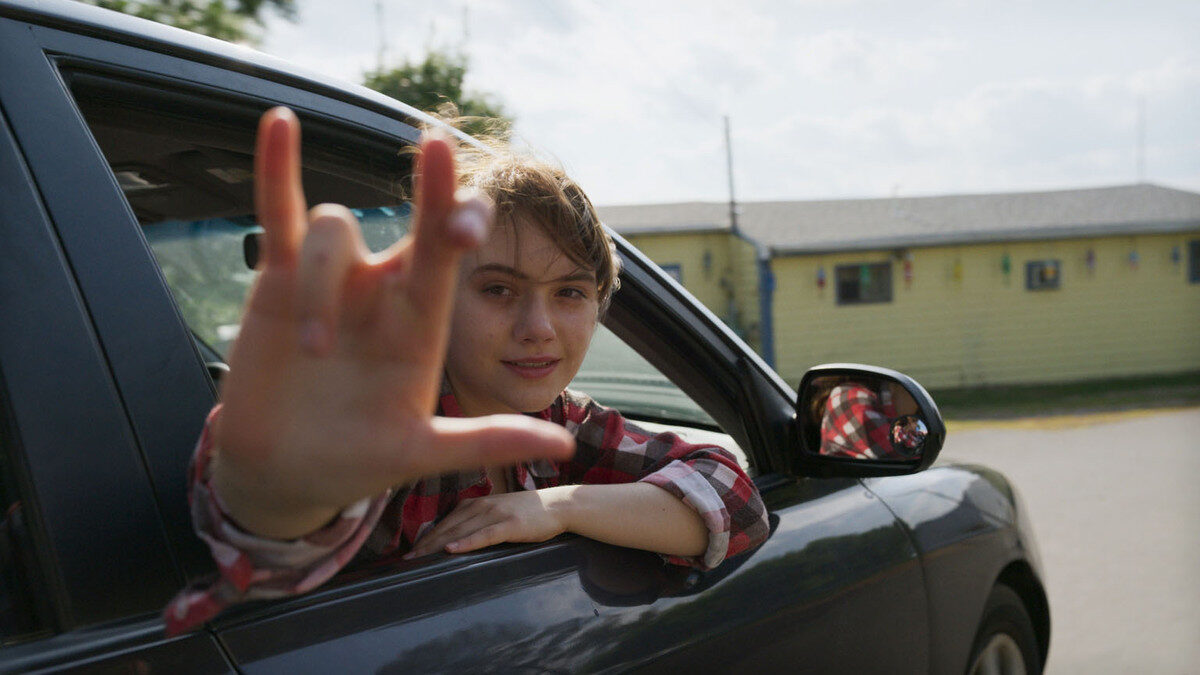 A protagonista do filme sorri com o corpo projetado para fora da janela de um carro em movimento